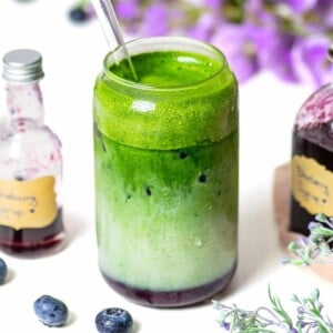 glass with blueberry syrup and matcha latte with small syrup bottle in background