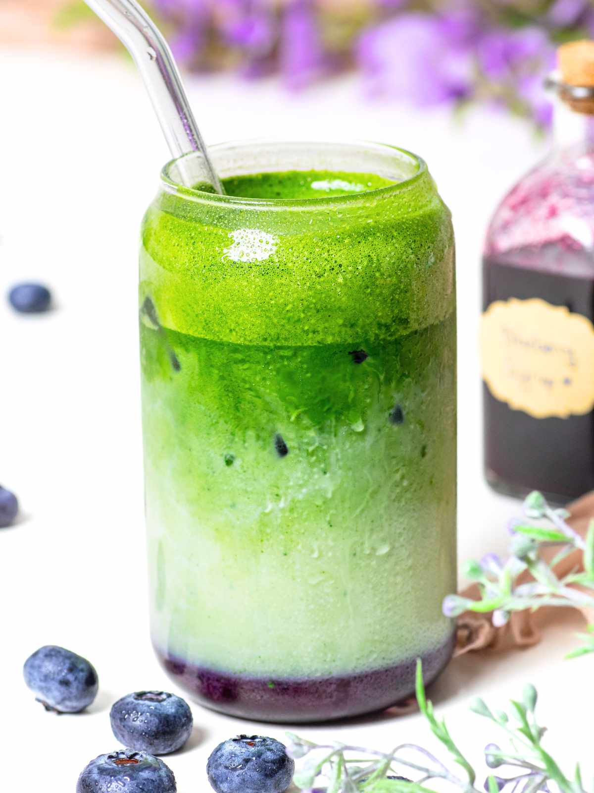glass with blueberry syrup and matcha latte with small syrup bottle in background