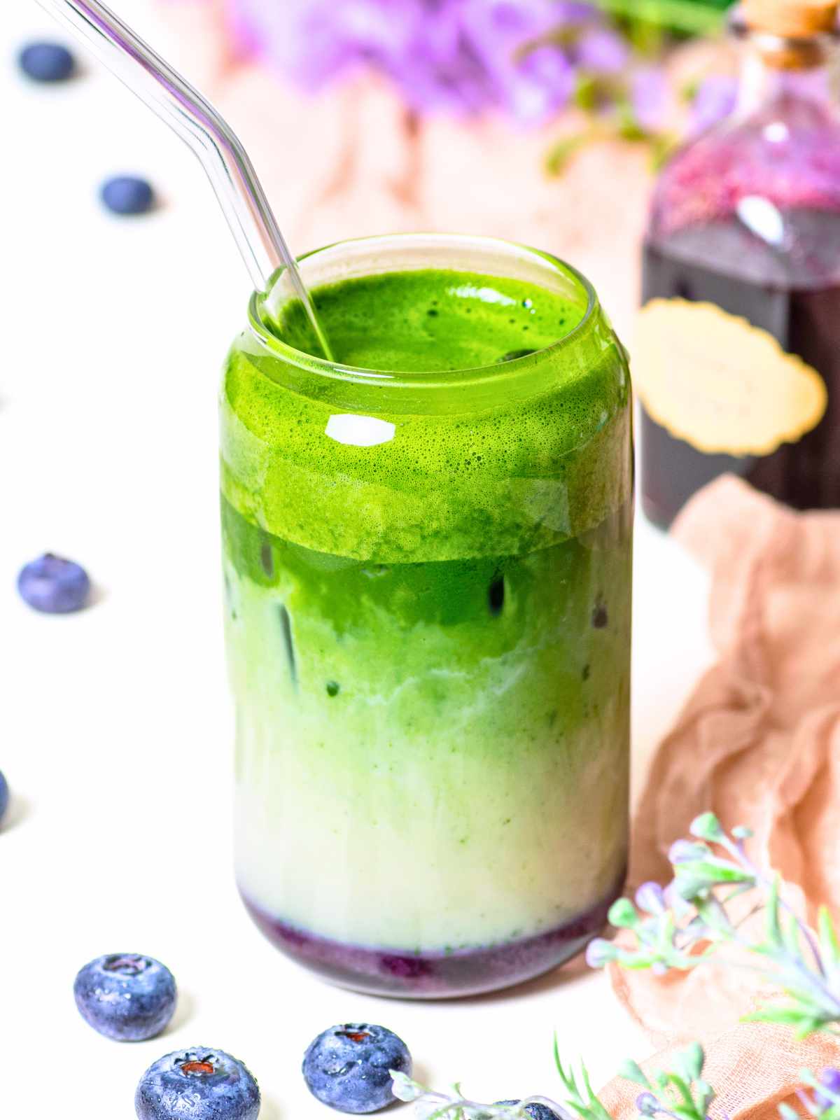 glass with blueberry syrup and matcha latte with small syrup bottle in background