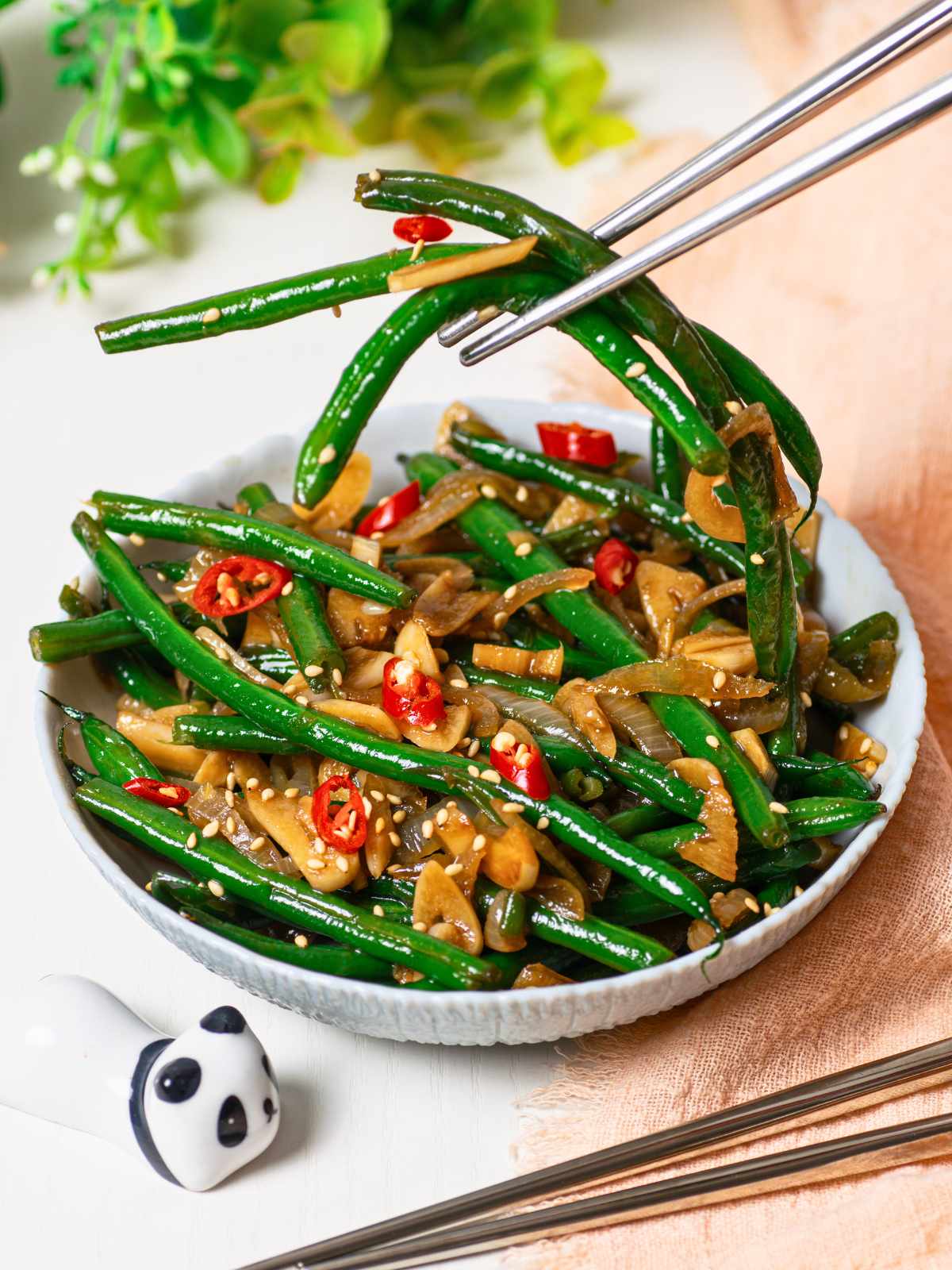 chopsticks over bowl of Korean green beans with onion and garlic and chili slices on top