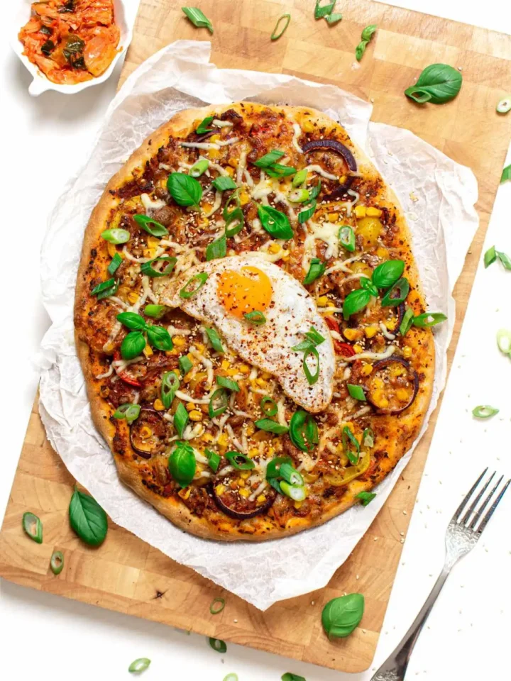 Kimchi pizza with fried egg on top on wooden board