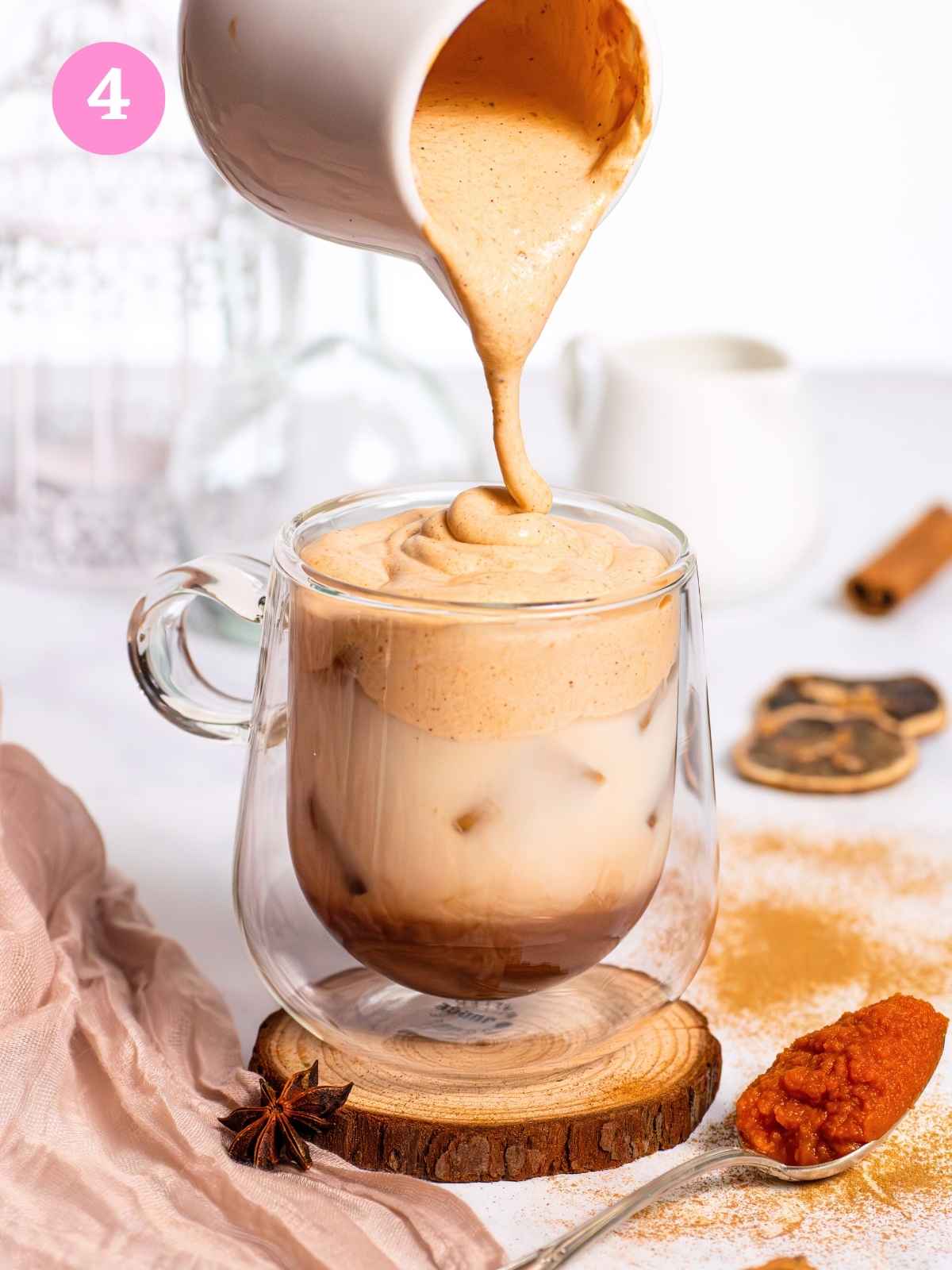 Pouring pumpkin spice cream over chai latte mixture in glass